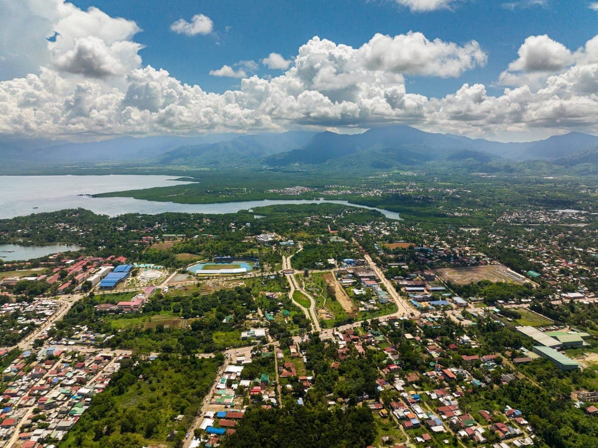 Aerial view of a coastal city with a bay, a sports stadium and mountains beyond