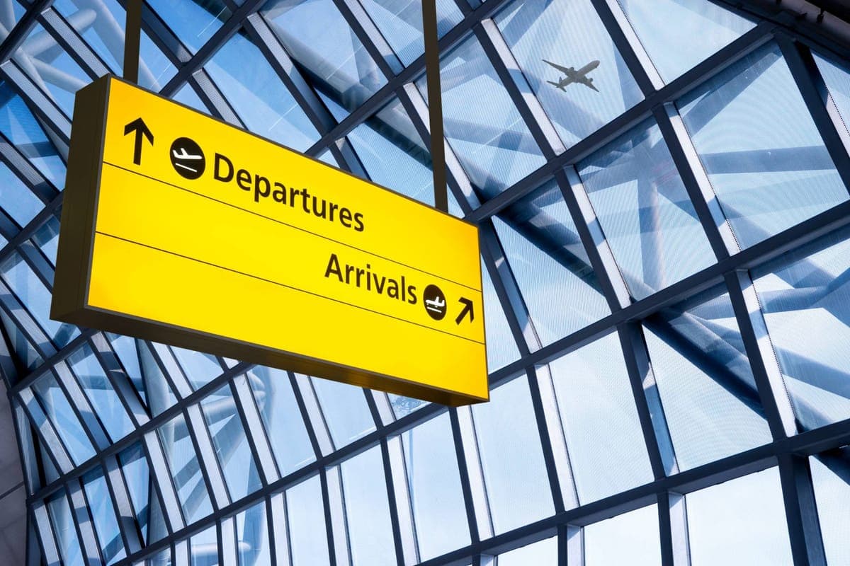 Yellow airport sign pointing to Departures and Arrivals, with an aircraft visible through the glass roof
